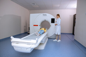 Little girl lying on table of mri scan machine female radiographer pushing button on control panel