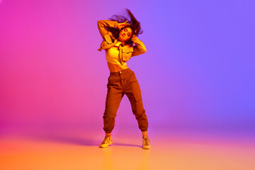 Flexible, artistic young girl, professional dancer in sport clothes dancing hip-hop against gradient pink purple background in neon light. Concept of contemporary dance, youth, hobby, action, motion