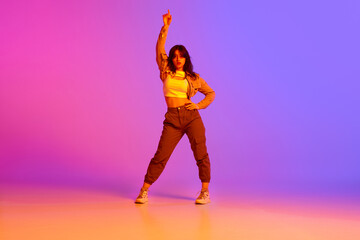 Beautiful young girl in sport style clothes dancing, making performance against gradient pink purple background in neon light. Concept of contemporary dance, youth, hobby, action and motion