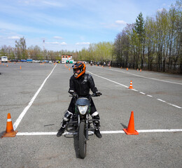 A young woman is learning to ride a motorbike in a motorcycle school. She is taught by a teacher.