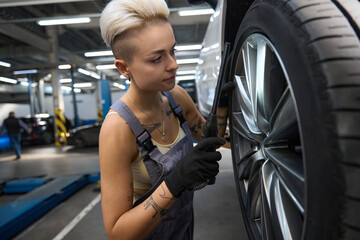 Fototapeta na wymiar Woman car mechanic in work overalls checks a car wheel