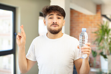 young handsome man crossing fingers and hoping for good luck. water bottle concept