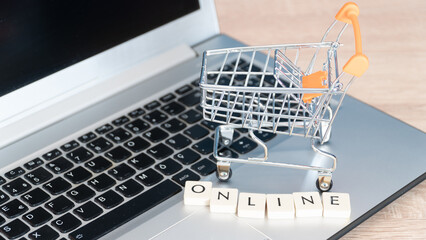 Online shopping concept. Black friday shopping online. Shopping cart or trolley and laptop on wooden table.