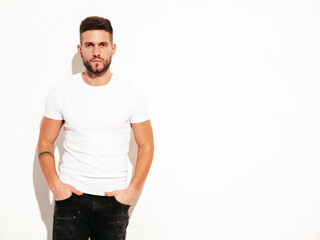 Fototapeta premium Portrait of handsome smiling stylish hipster lambersexual model. Man dressed in white T-shirt and jeans. Fashion male posing in studio