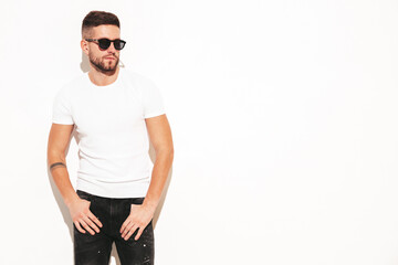 Portrait of handsome smiling stylish hipster lambersexual model. Man dressed in white T-shirt and jeans. Fashion male posing in studio