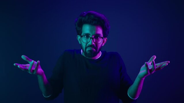 Studio dark blue neon background Indian man Arabian male model guy confused shrug shoulders unsure doubtful shrugging doubt uncertain don't know problem solution question guess puzzled bemused no clue