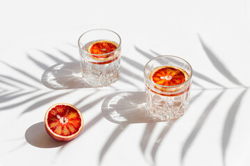 Creative composition made of half bloody red orange and two glasses with cocktail on white...