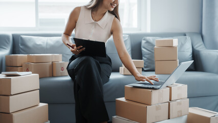 Using laptop, Portrait of pretty asian sme freelancer woman checking customer paid order on sofa after packing into cardboard box, online home small business, online influencer asia people.