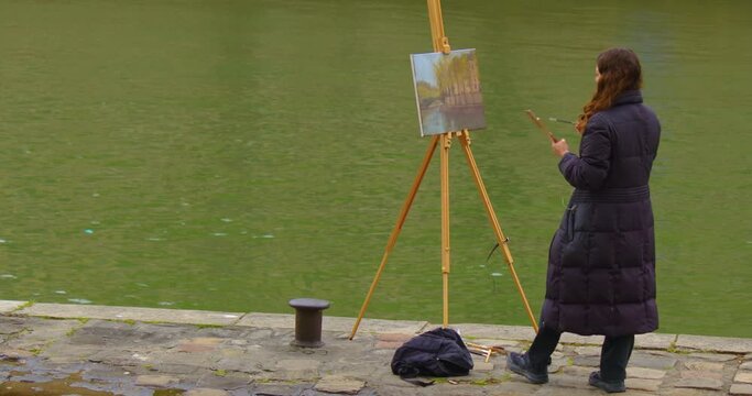 Female street art painter has some sketch practice with Paris city landscape. Experienced European woman artist draws new painting near the river. Painter and her lifestyle hobby leisure