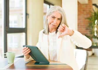 senior pretty woman feeling cross,showing thumbs down with a touch screen