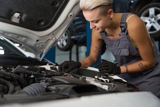 Young woman in work overalls repairs a car engine