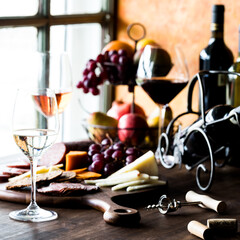 A table top scene of assorted wine and cheese against a bright window.