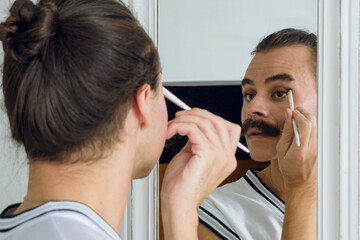 reflection in the mirror of a non-binary person putting makeup on their eyelids with a small brush
