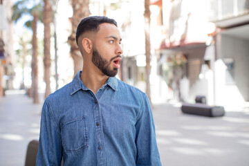 young handsome man feeling shocked and surprised, looking to copy space on the side with amazed, open-mouthed look