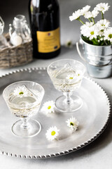 Two glasses of white wine with daisy flower blossoms on a metal tray.