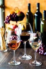 Glasses of rose, red and white wine with wine bottles and fruit in behind.