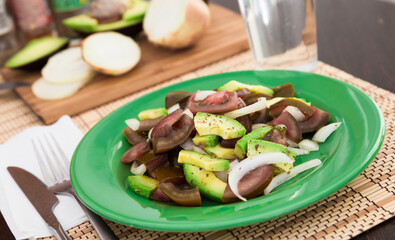 salad of black tomatoes, avocado and onions on green plate