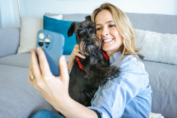 Young beautiful woman having great time with her little sweet dog at home, taking many pictures. Lifestyle and friendship concept.