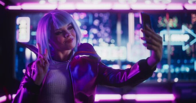 Portrait of a Beautiful Content Creator Taking Selfie Photos on Smartphone. Young Female Making Cyberpunk Cosplay in Stylish Clothes and Blue Hair. Gamer Female Standing in Futuristic Neon Room