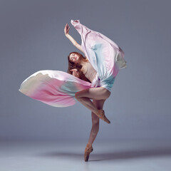 Weightless easy jump. Sensual ballerina with dancing with fabric over grey studio background....