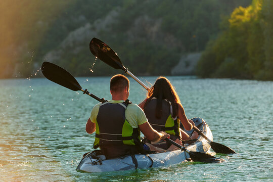 A young couple enjoying an idyllic kayak ride in the middle of a beautiful river surrounded by forest greenery in sunset time 