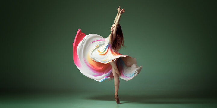 Portrait with one young woman, classic dancer dancing in colorful painted dress over dark green background. Contemporary dance style, ballet