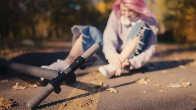 Young woman fell off an e-scooter, rubbing hurt foot, injury, outdoor accident
