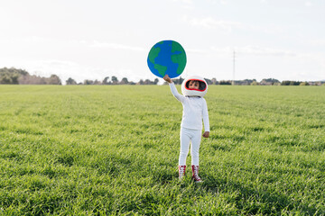 Girl wearing astronaut costume holding cut out of earth standing on grass