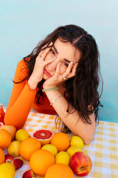 Young woman touching face with citrus fruits on table