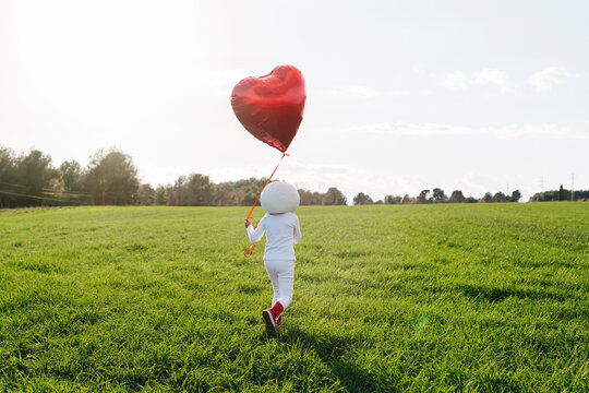 Girl dressed as astronaut walking on meadow holding heart shape balloon