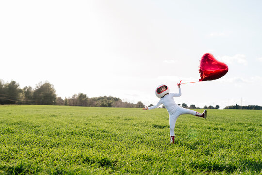 Playful girl holding heart shape balloon standing on grass