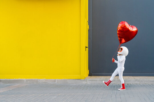 Girl holding heart shape balloon walking near yellow wall