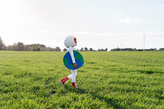 Girl dressed as astronaut walking with earth cut out on grass