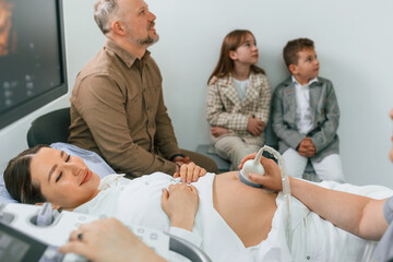 Family is sitting together. Pregnant woman is lying down in the hospital, doctor does ultrasound