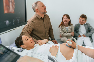 Obraz premium Husband and kids are sitting together. Pregnant woman is lying down in the hospital, doctor does ultrasound