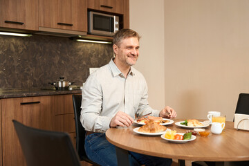 Side view happy man having delicious breakfast in the kitchen in hotel room
