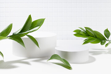 White contemporary fresh stage with two cylinder podiums mockup, tiny tile wall, bright tropical green leaves in summer hard light with shadows for presentation cosmetic products, goods, design.