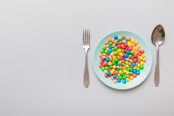 cutlery on table and sweet plate of candy. Health and obesity concept, top view on colored background