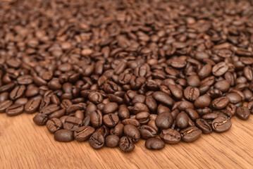 Heap of fresh roasted coffee beans on the brown wooden table. Close-up. Selective focus. 
