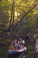 A young couple enjoying an idyllic kayak ride in the middle of a beautiful river surrounded by forest greenery