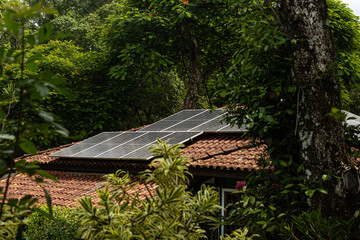 Placas solares instaladas em telhado de uma grande casa sustentável no meio de extensa vegetação.