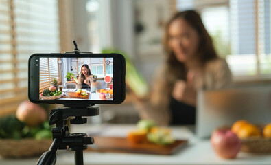 Beautiful young female health coach recording on a smart phone her vlog about healthy eating. - obrazy, fototapety, plakaty
