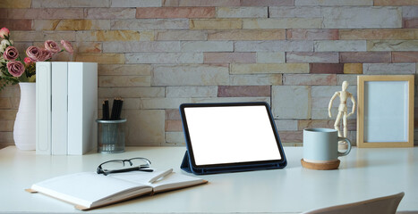Digital tablet with empty display, glasses, notebook and coffee cup in white table.
