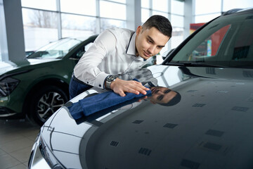Fototapeta na wymiar Young consultant in a car dealership wipes the hood of a car