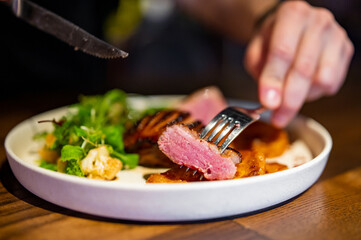 man with a knife and fork cuts grilled duck meat