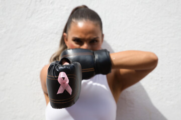 Young beautiful woman with boxing gloves with pink ribbon against breast cancer and white top on...
