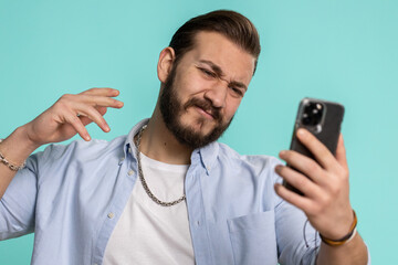 Lebanese man use mobile cell phone typing browsing, loses becoming surprised sudden lottery results, bad fortune, loss, fail. Handsome arabian guy isolated alone on blue studio wall background indoors