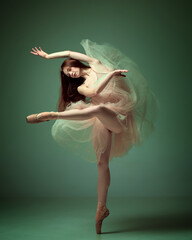 Sensual red haired ballerina wearing tulle dress dancing with emotions over dark green studio...