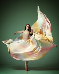 Portrait with one young girl, beautiful ballerina wearing silk dress spinning in dance over dark green studio background © Lustre Art Group 