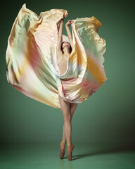 Ballerina wearing colorful dress dancing elegant movements with fabric over dark green studio background. Showing flexibility and grace © Lustre Art Group 